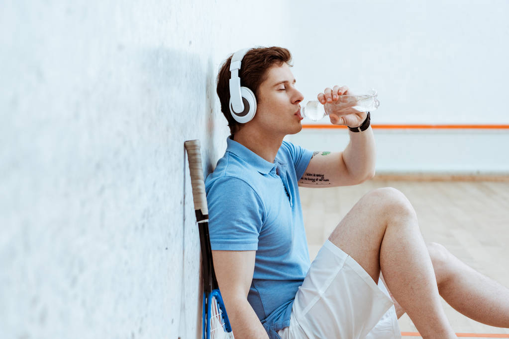 Joueur de squash écoutant de la musique dans les écouteurs et l'eau potable
 - Photo, image