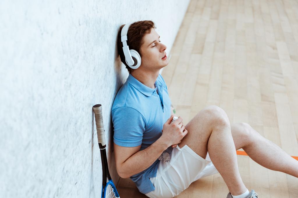 Squash oyuncu katta oturan ve kapalı gözlerle müzik dinleme - Fotoğraf, Görsel