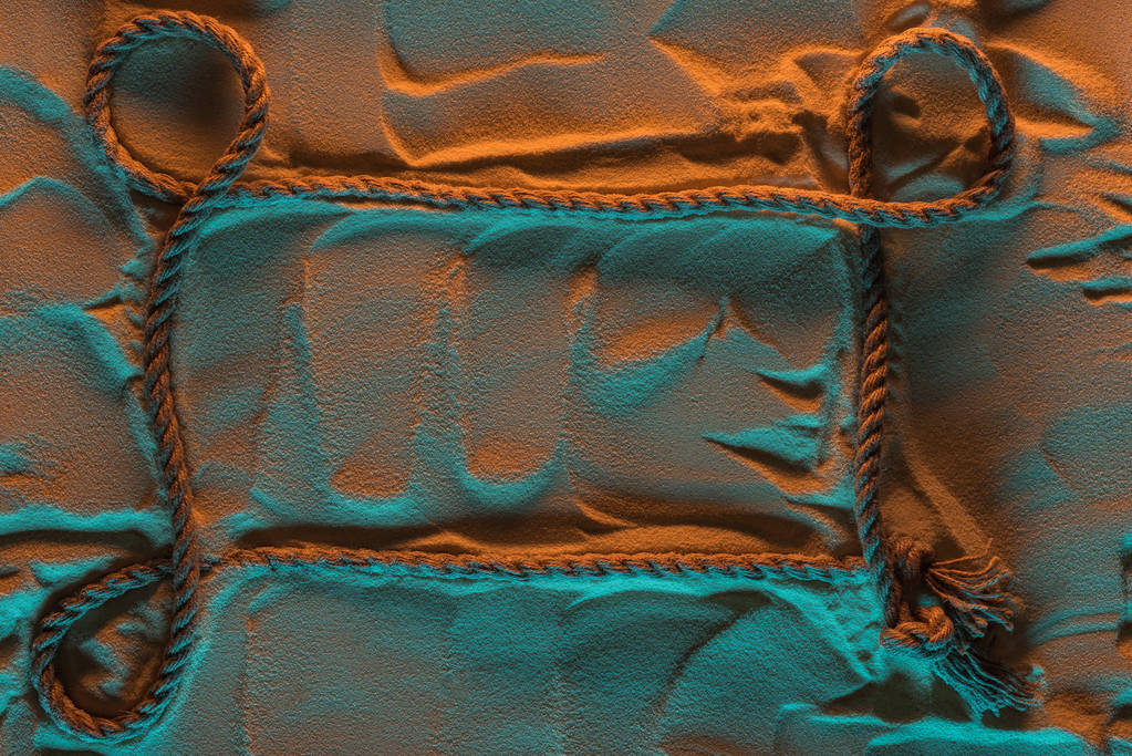 Draufsicht auf Seil mit Knoten auf Sand mit orangefarbenen und blauen Lichtern und Kopierraum - Foto, Bild