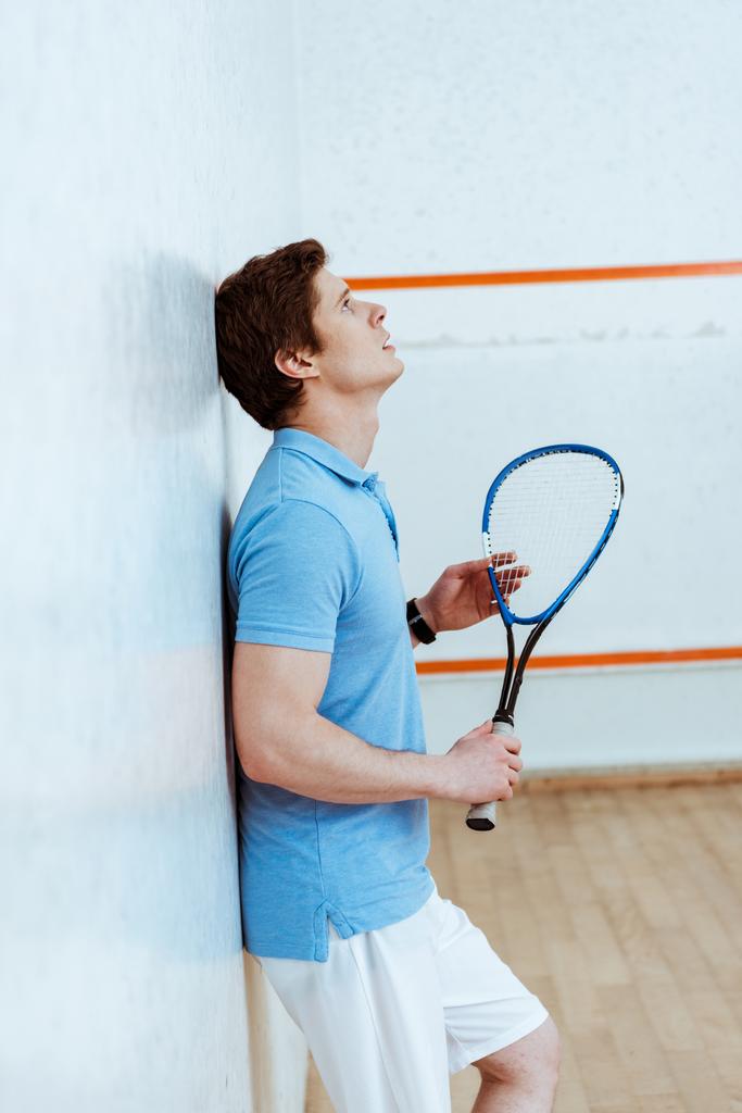 Vista lateral do triste jogador de squash segurando raquete em quadra de quatro paredes
 - Foto, Imagem