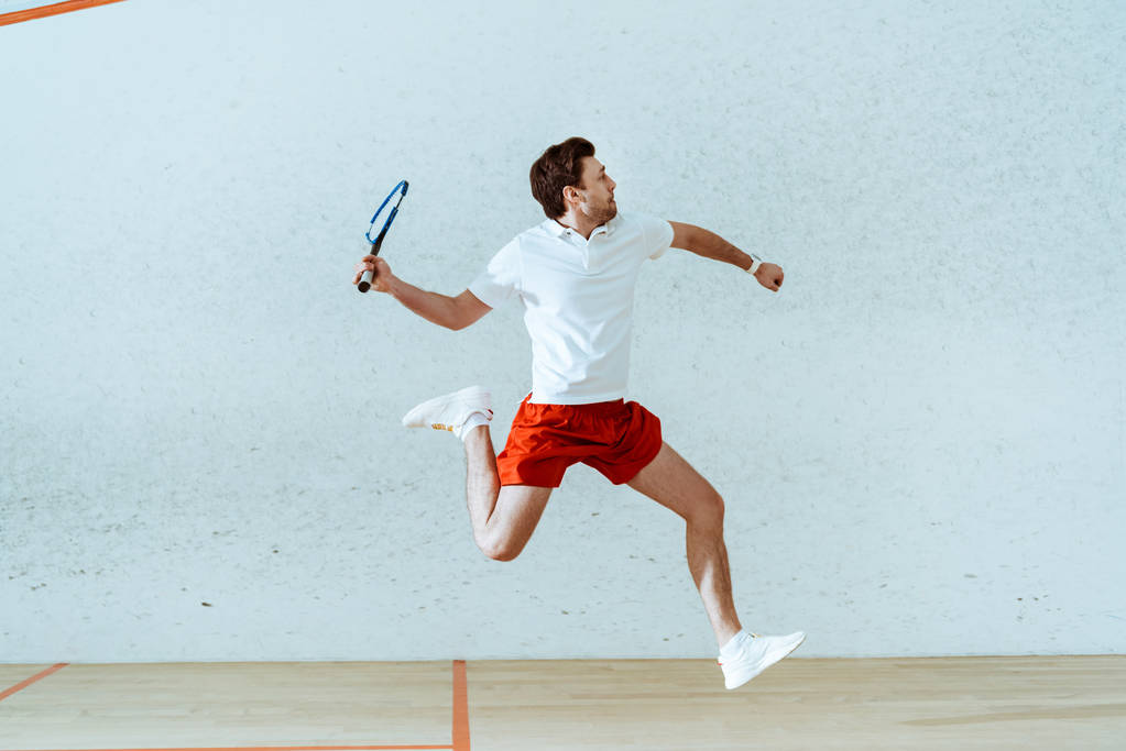 Esportista de camisa de pólo pulando enquanto joga squash em quadra de quatro paredes
 - Foto, Imagem