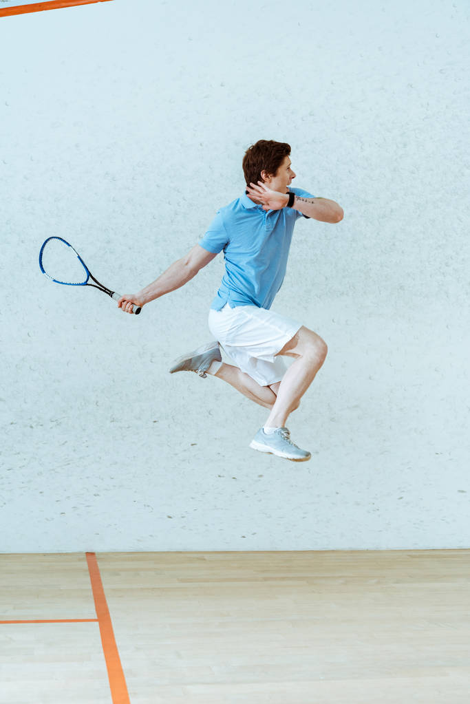Спортсмен у сорочці поло стрибає під час гри в сквош у чотиристоронньому дворі
 - Фото, зображення