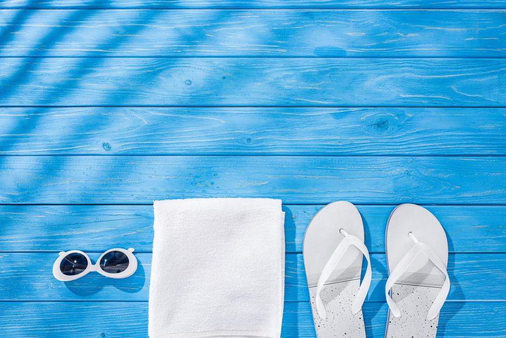 vista superior de toalla blanca plegada, gafas de sol retro y chanclas sobre fondo de madera azul con sombras y espacio para copiar
 - Foto, imagen