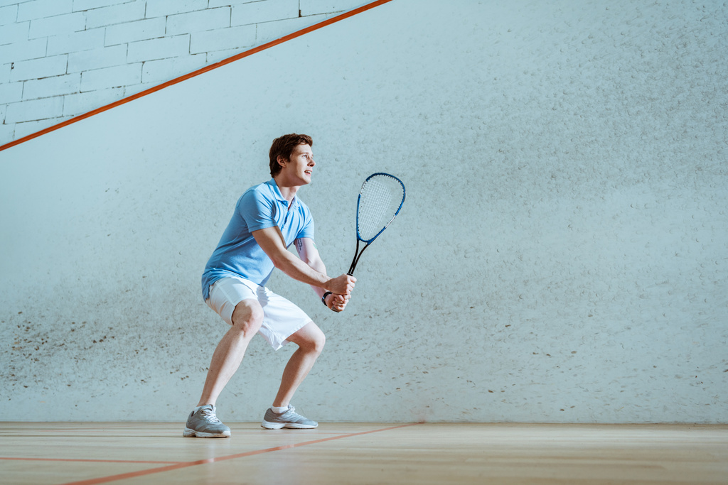 Vista completa del deportista concentrado en polo azul jugando squash
 - Foto, Imagen