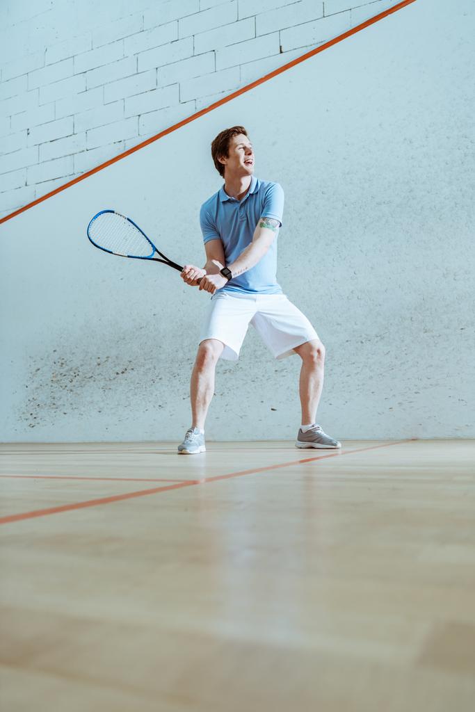 Ganzkörperansicht des konzentrierten Sportlers im blauen Poloshirt beim Squash - Foto, Bild
