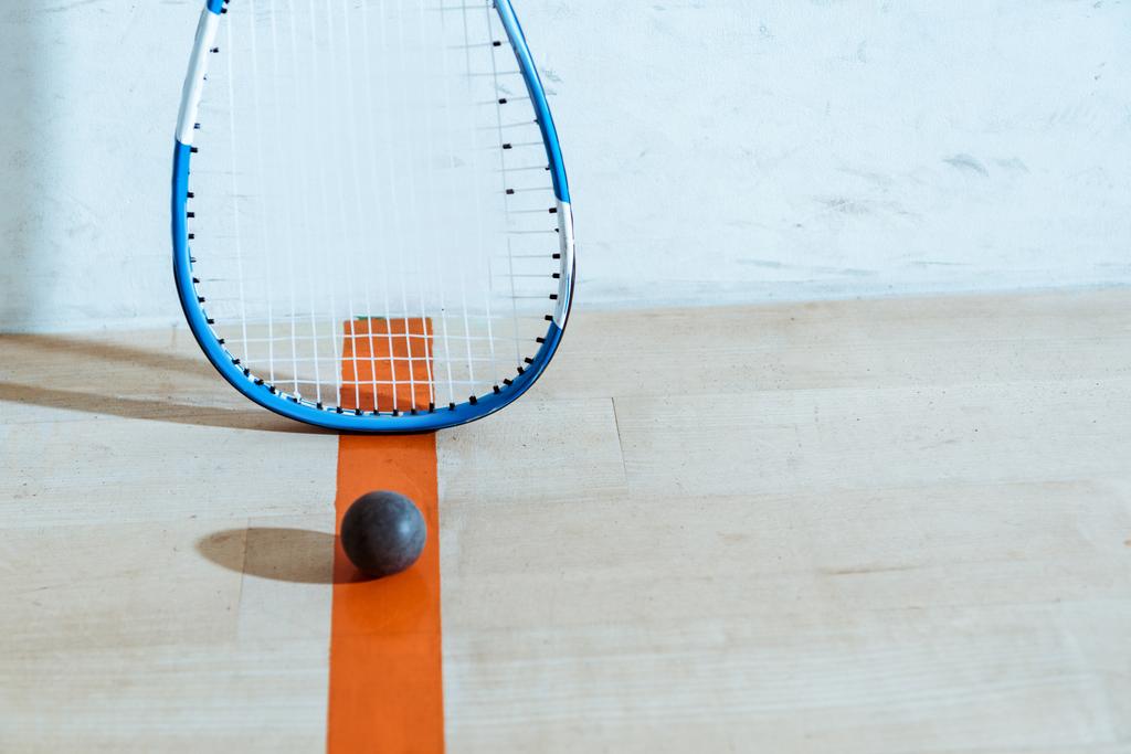 Squashová raketa a míč na dřevěné podlaze v nádvoří se čtyřmi stěnami - Fotografie, Obrázek