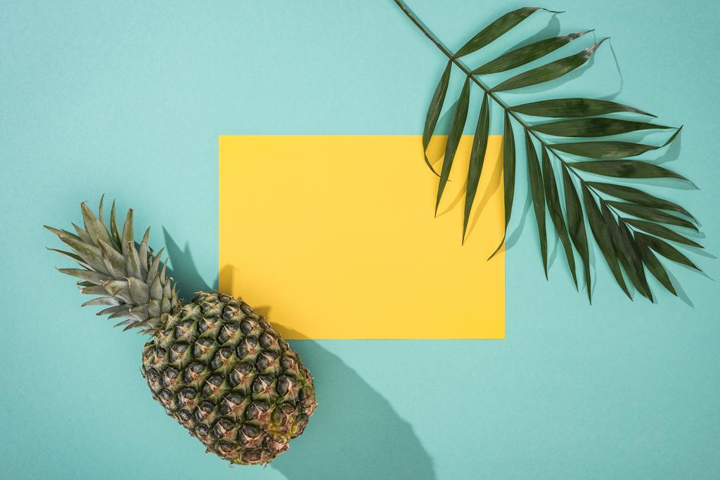 top view of pineapple, tropical leaf and yellow card with copy space on turquoise background - Photo, Image
