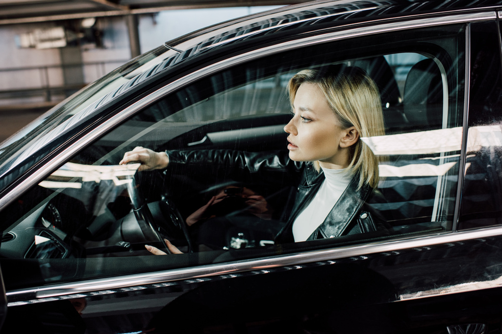 車を運転しながらステアリングホイールを保持している魅力的なブロンドの女性  - 写真・画像