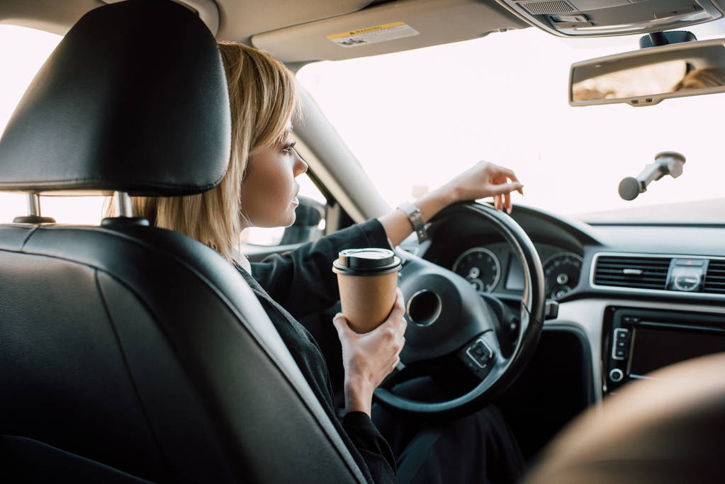 mujer joven rubia sosteniendo taza de papel mientras está sentado en el coche
  - Foto, Imagen