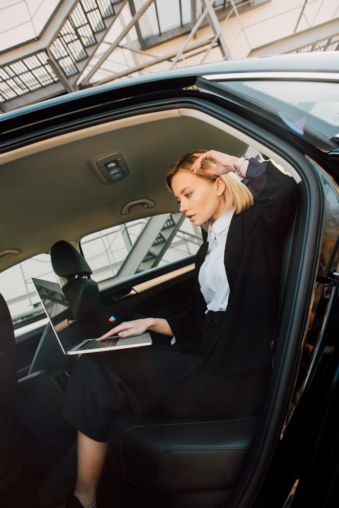 beautiful blonde young woman using laptop while sitting in car  - Photo, Image