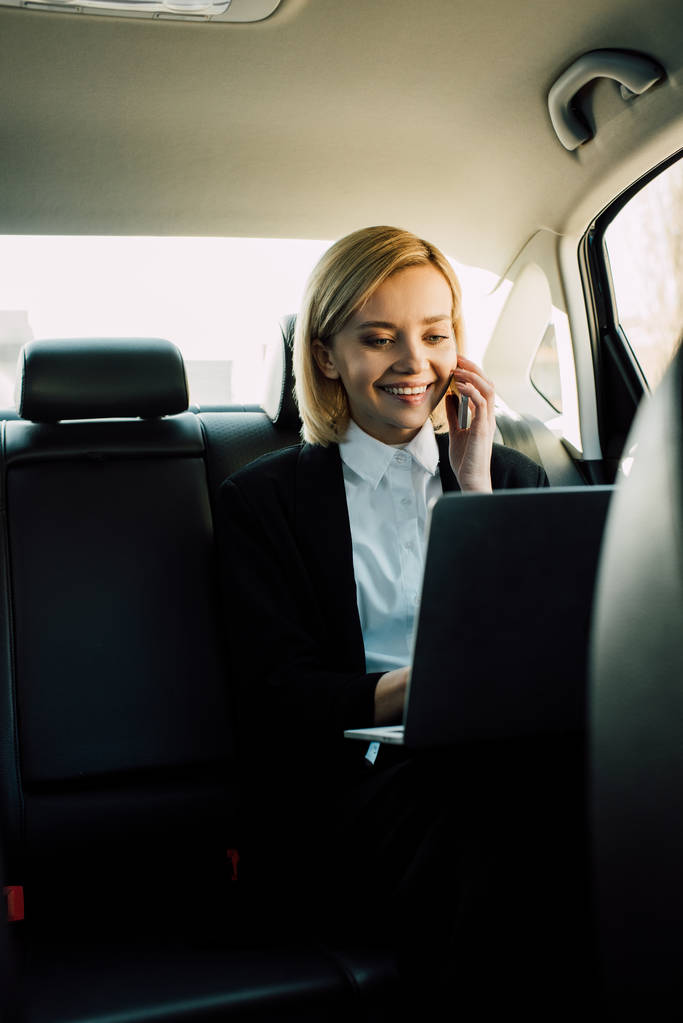 femme blonde souriante parlant sur smartphone et regardant un ordinateur portable en voiture
  - Photo, image