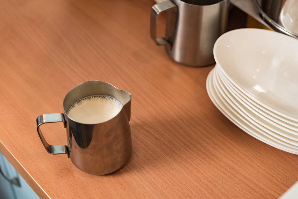Brocche in acciaio con latte e piatti sul tavolo di legno
 - Foto, immagini