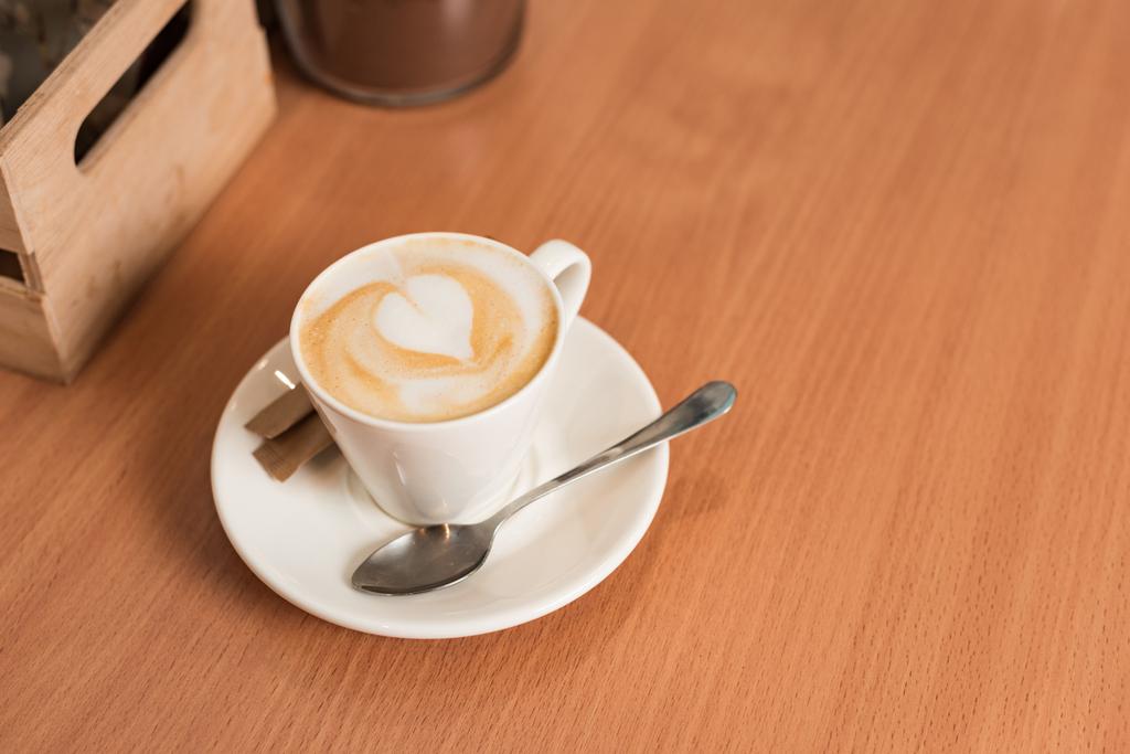 Šálek kávy s talířem a lžičkou na dřevěném stole - Fotografie, Obrázek