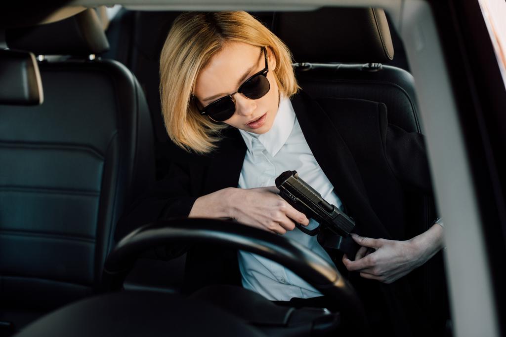 車の中で銃を持つサングラスで危険なブロンドの女性  - 写真・画像