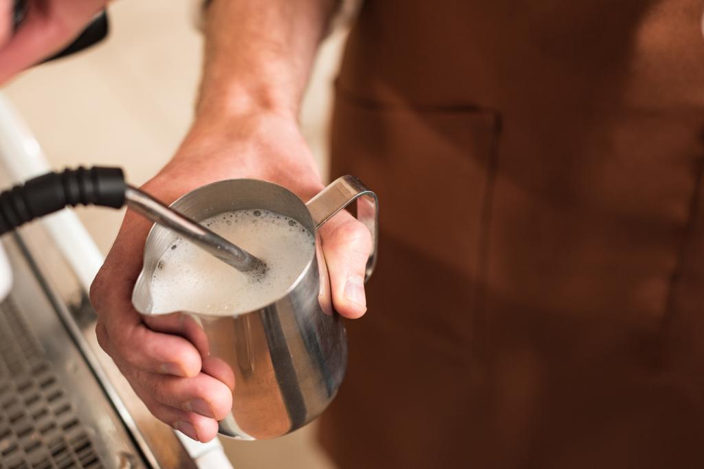 Vista cortada de barista enchendo jarro de leite de aço
 - Foto, Imagem