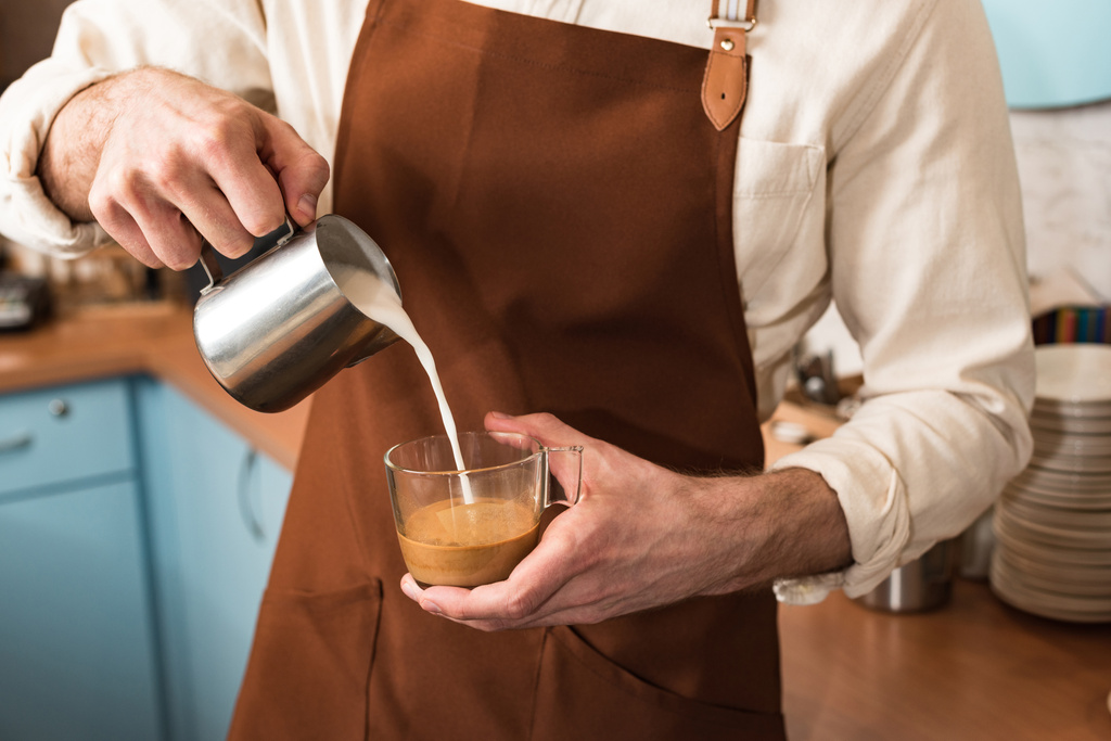 Περικομμένη θέα του μπάρμαν που ρίχνει γάλα στον καφέ - Φωτογραφία, εικόνα