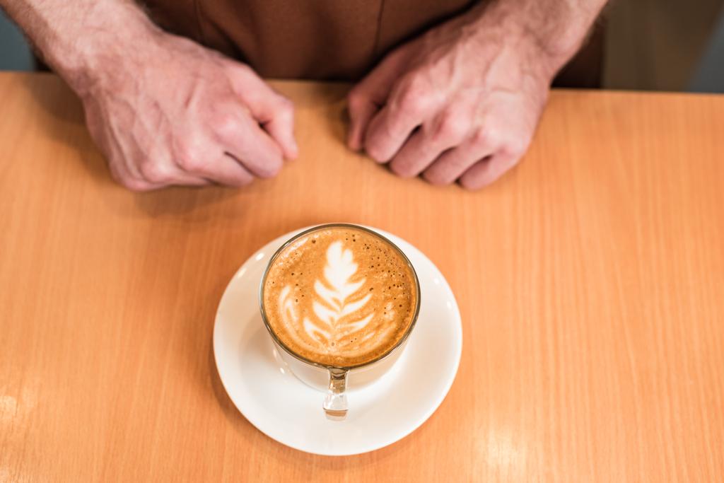 Vista parcial de barista con taza de café sobre mesa de madera
 - Foto, Imagen