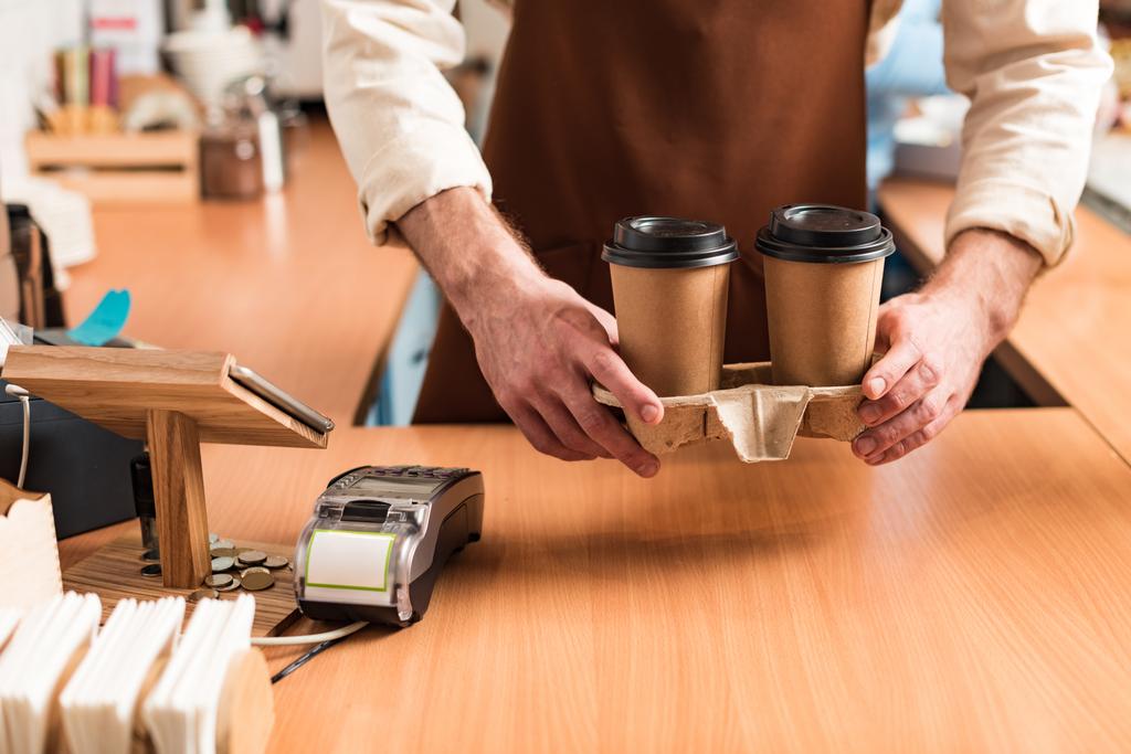 Cropped view of barista in brown apron holding take-out cup carrier with coffee - Photo, Image