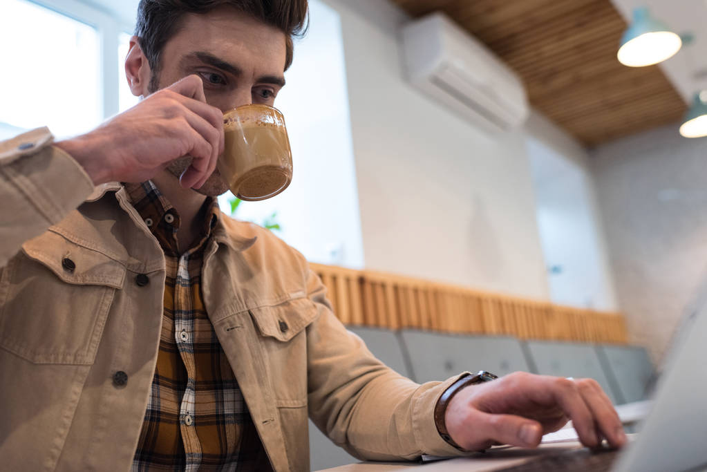 Freelancer bebiendo café y usando laptop en cafetería
 - Foto, Imagen