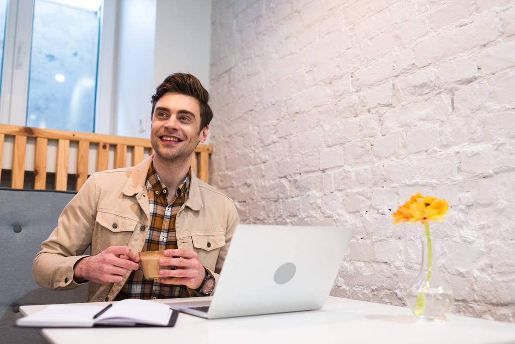 Freelancer sorridente com laptop segurando xícara de café no café
 - Foto, Imagem