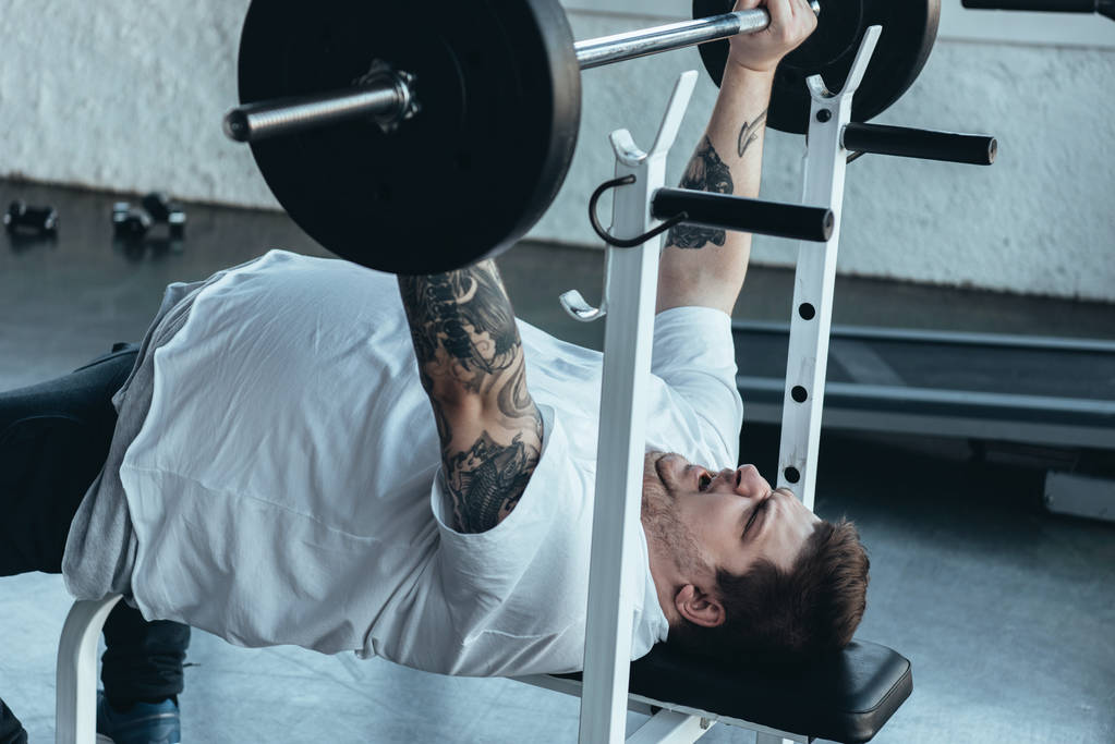 Túlsúlyos tetovált ember, fehér póló gyakorlása a súlyzó a tornaterem - Fotó, kép