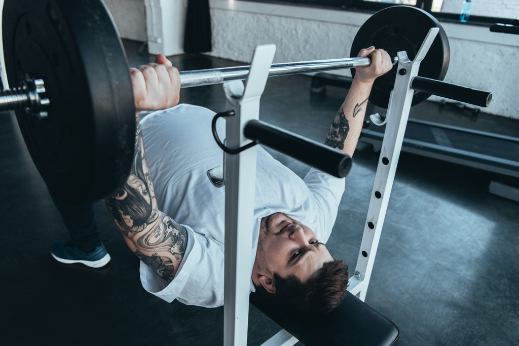 Uomo obeso tatuato in t-shirt bianca allenamento con bilanciere in palestra
 - Foto, immagini