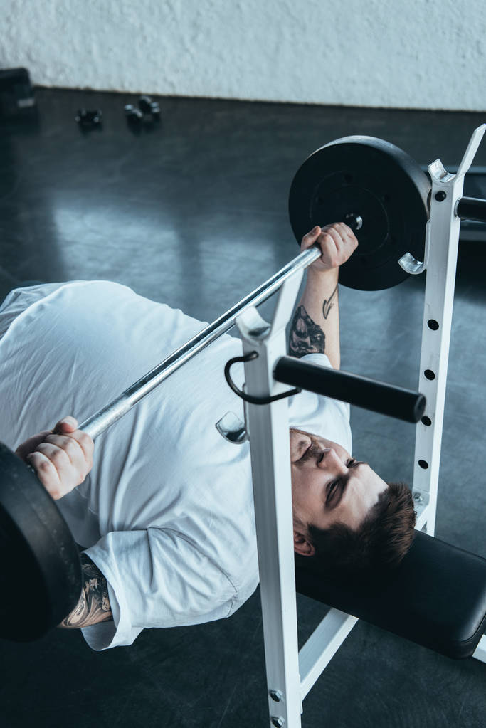 Ожирний татуйований чоловік тренується з барбелом у спортзалі
 - Фото, зображення