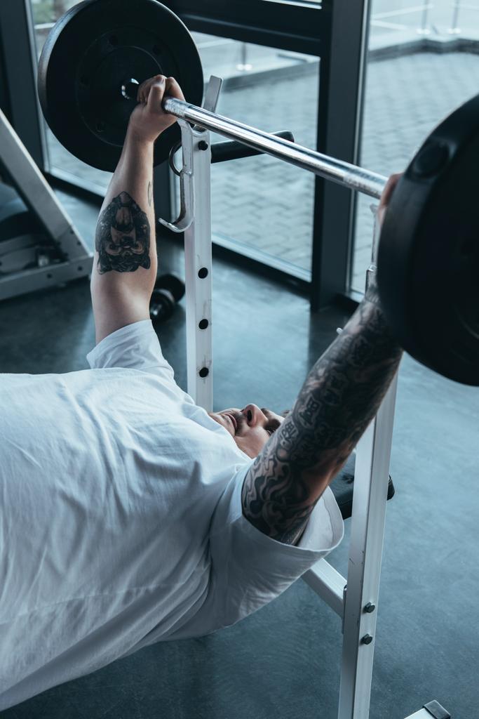 Overweight tattooed man training with barbell at gym - Photo, Image