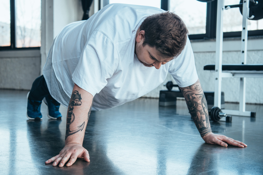 overweight tattooed man doing push up exercise at sports center - Photo, Image