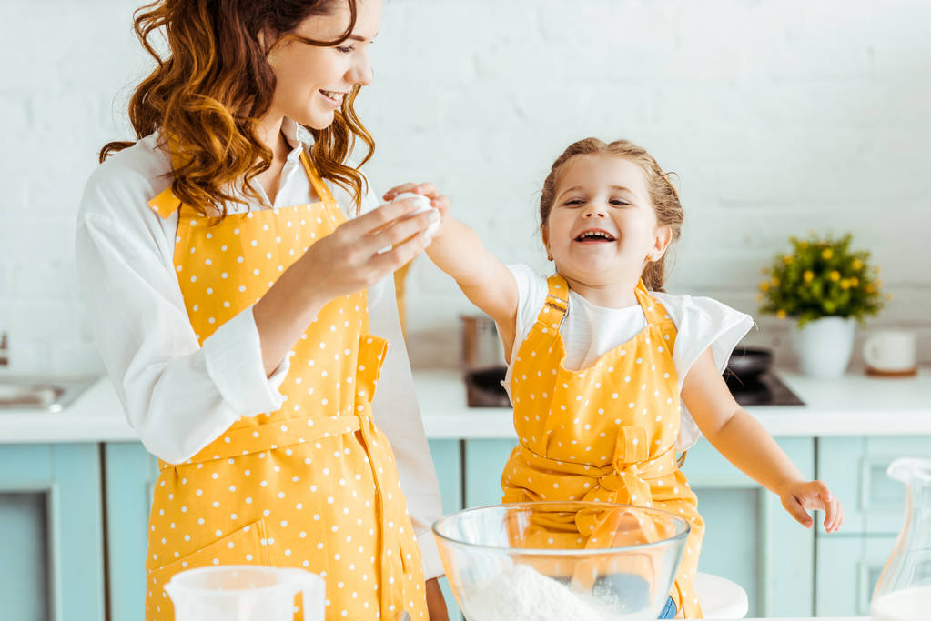 podekscytowany emocjonalna córka gospodarstwa jajko z matką w żółtym polka dot fartuch w kuchni - Zdjęcie, obraz
