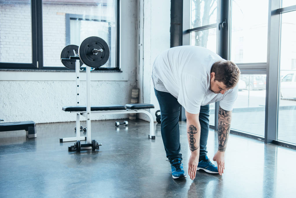 elhízott ember tetovált fehér póló csinál stretching gyakorolni sportközpont - Fotó, kép