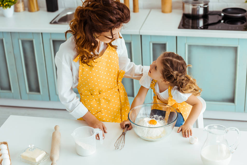 мать и дочь в фартуках смотрят друг на друга, пока готовят вместе на кухне
 - Фото, изображение
