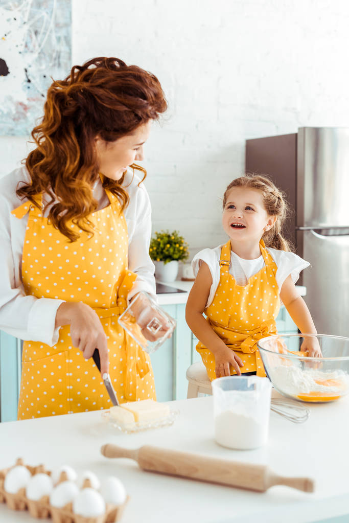 селективное внимание женщины режет масло и смотрит на счастливую дочь на кухне
 - Фото, изображение