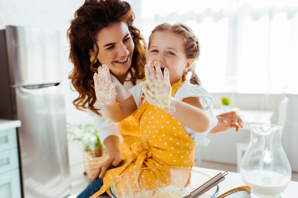 lachende moeder kijkt naar lachen dochter met vuile handen in het deeg - Foto, afbeelding