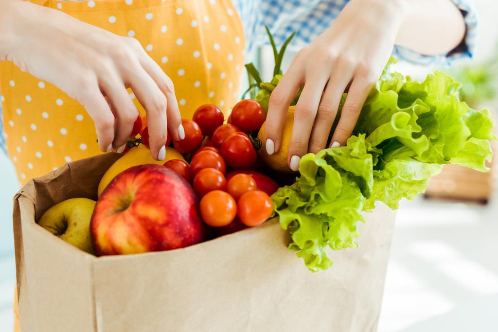 částečné zobrazení ženy dotek čerstvého zralých plodů a zeleniny v papírové tašce - Fotografie, Obrázek