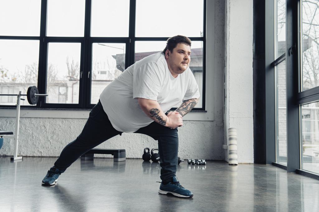 Übergewichtiger tätowierter Mann streckt Beine im Sportzentrum - Foto, Bild