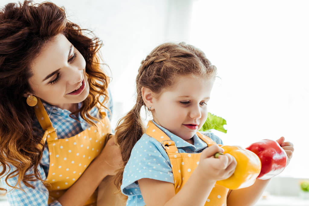 mère heureuse regardant sa fille tenant des poivrons rouges et jaunes
 - Photo, image