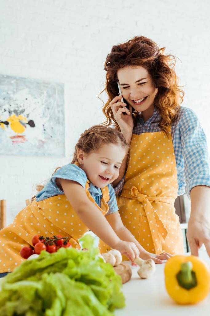 foyer sélectif mère heureuse parlant sur smartphone près de fille souriante toucher les champignons
 - Photo, image