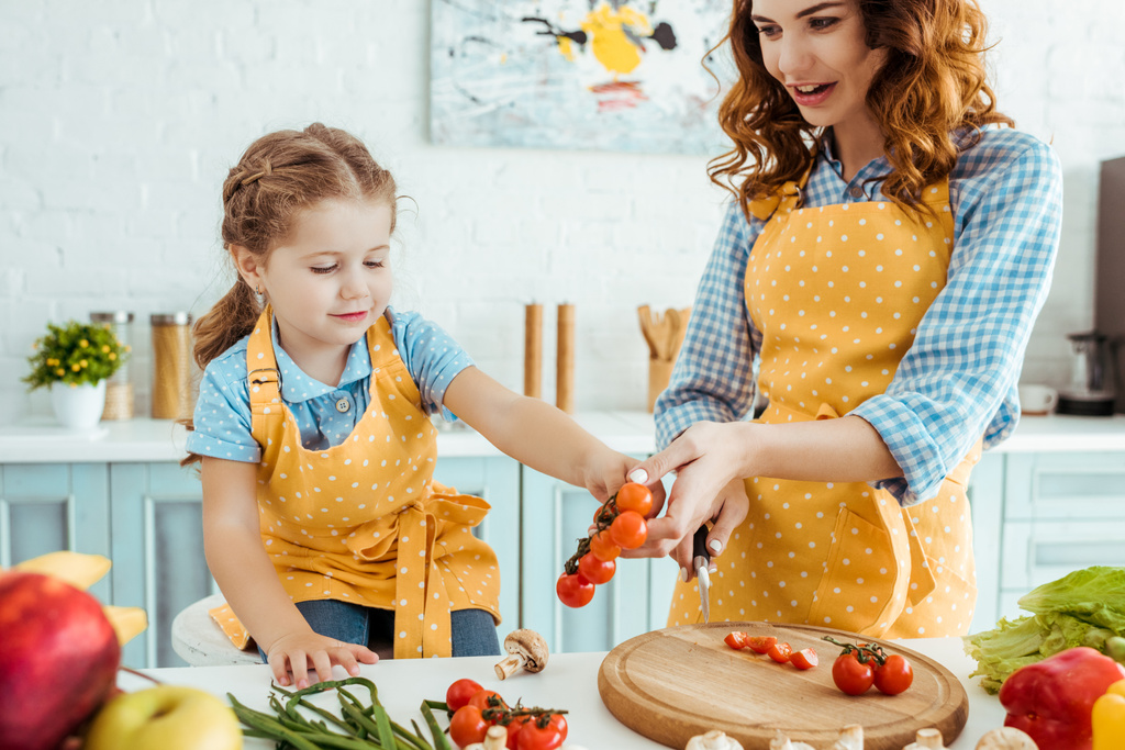  dochter in polka dot gele schort geven cherry tomaten aan moeder - Foto, afbeelding