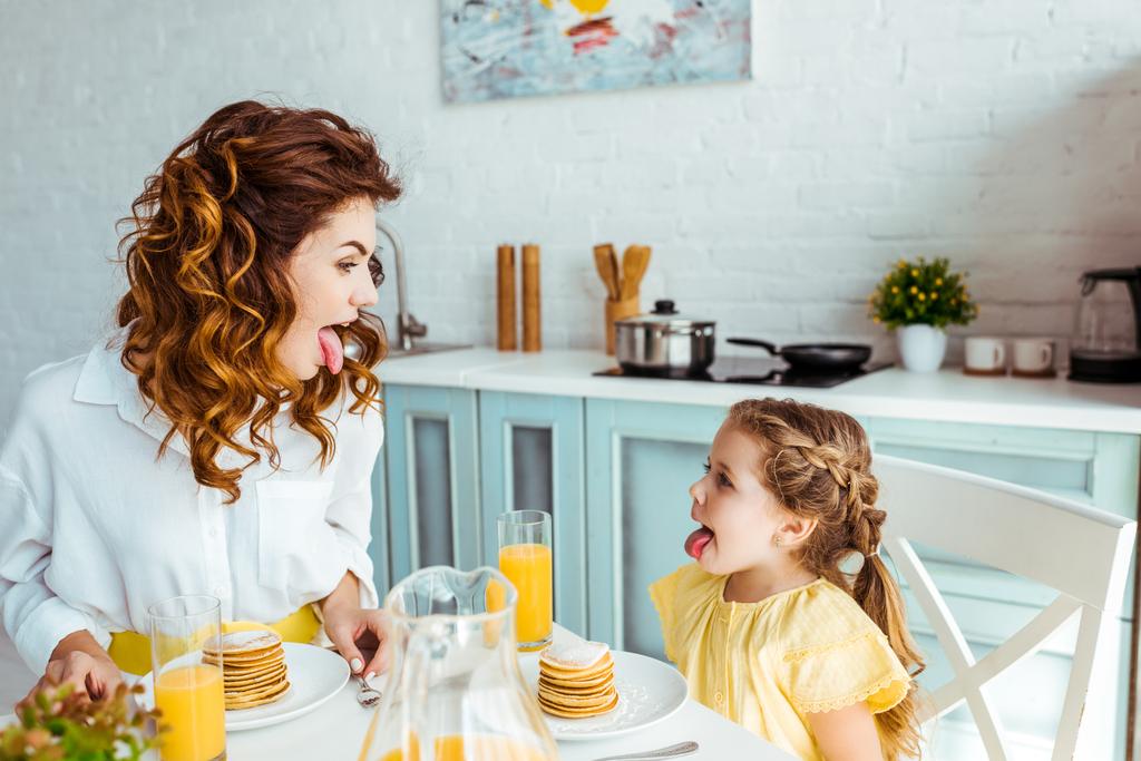 hauska tytär ja äiti törröttää kielet aamiaisen aikana
 - Valokuva, kuva