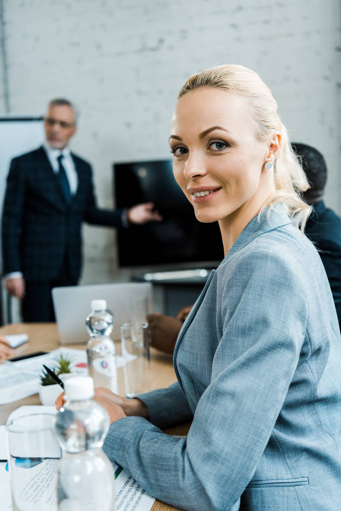 foco seletivo de mulher de negócios loira feliz perto de treinador de negócios na sala de conferências
  - Foto, Imagem