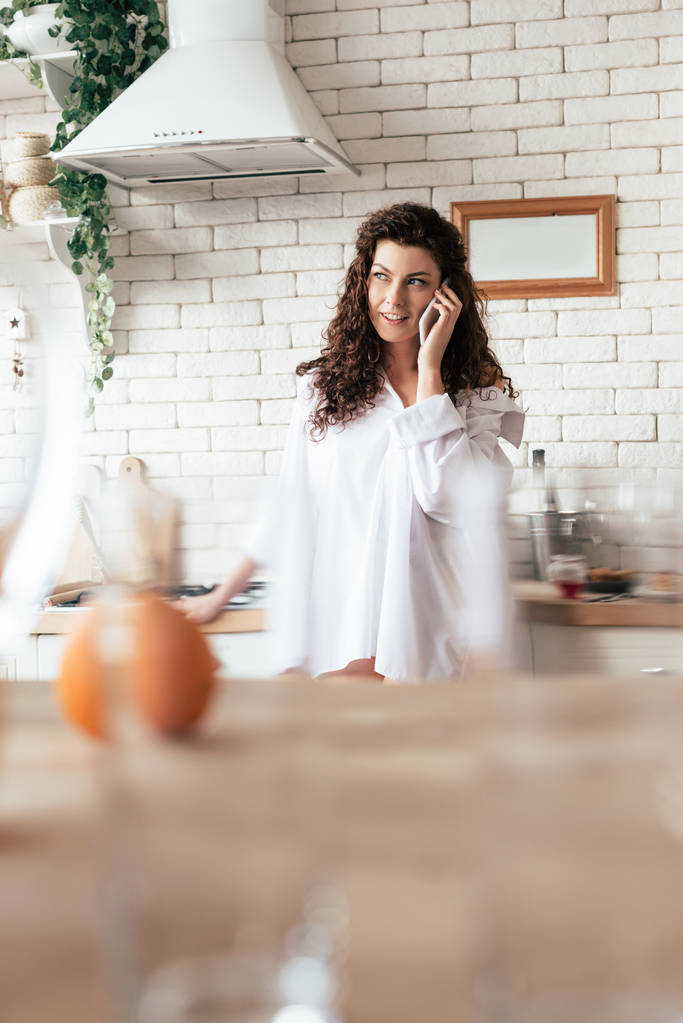 akıllı telefon konuşuyor ve mutfakta uzağa bakarak beyaz gömlekli çekici kız - Fotoğraf, Görsel