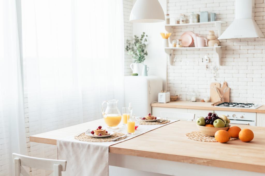 served table with pancakes, fruits and orange juice in kitchen - Photo, Image