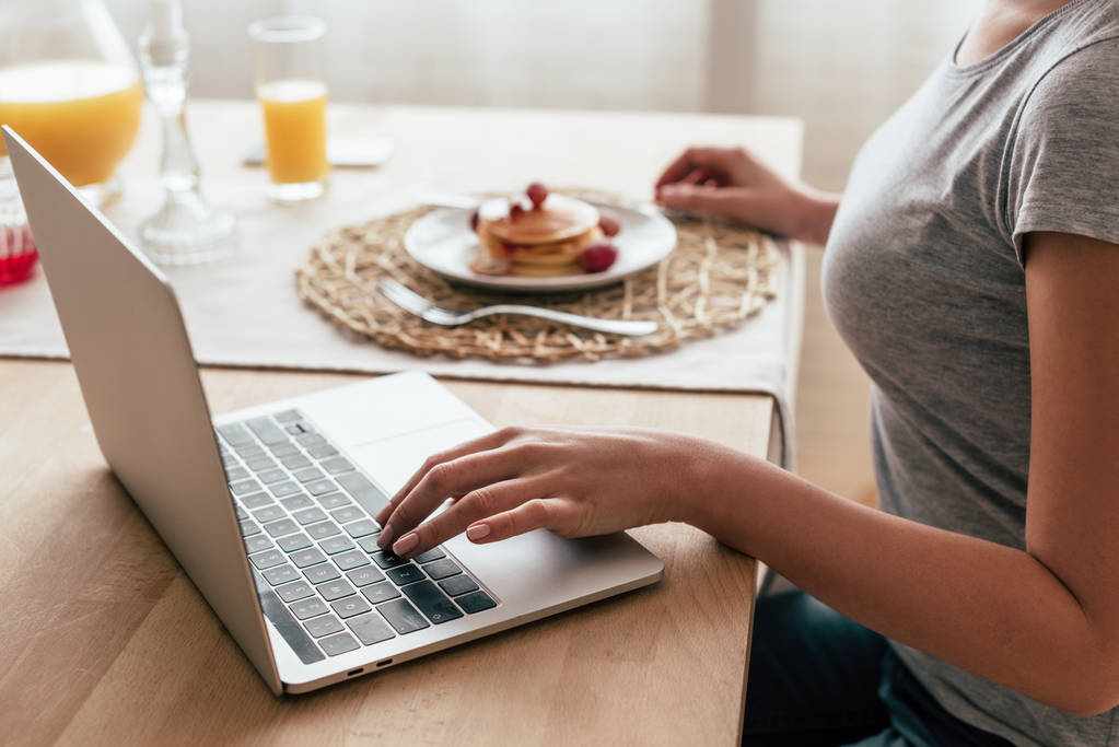 vista parziale della donna che utilizza il computer portatile durante la colazione
 - Foto, immagini