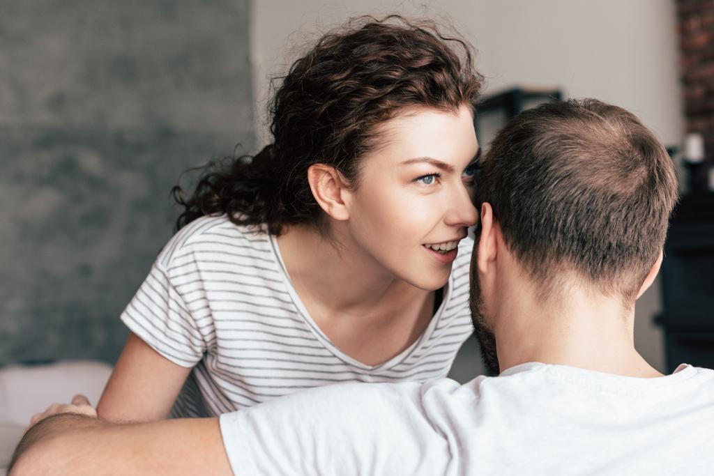 beautiful curly girl whispering to boyfriend at home - Photo, Image