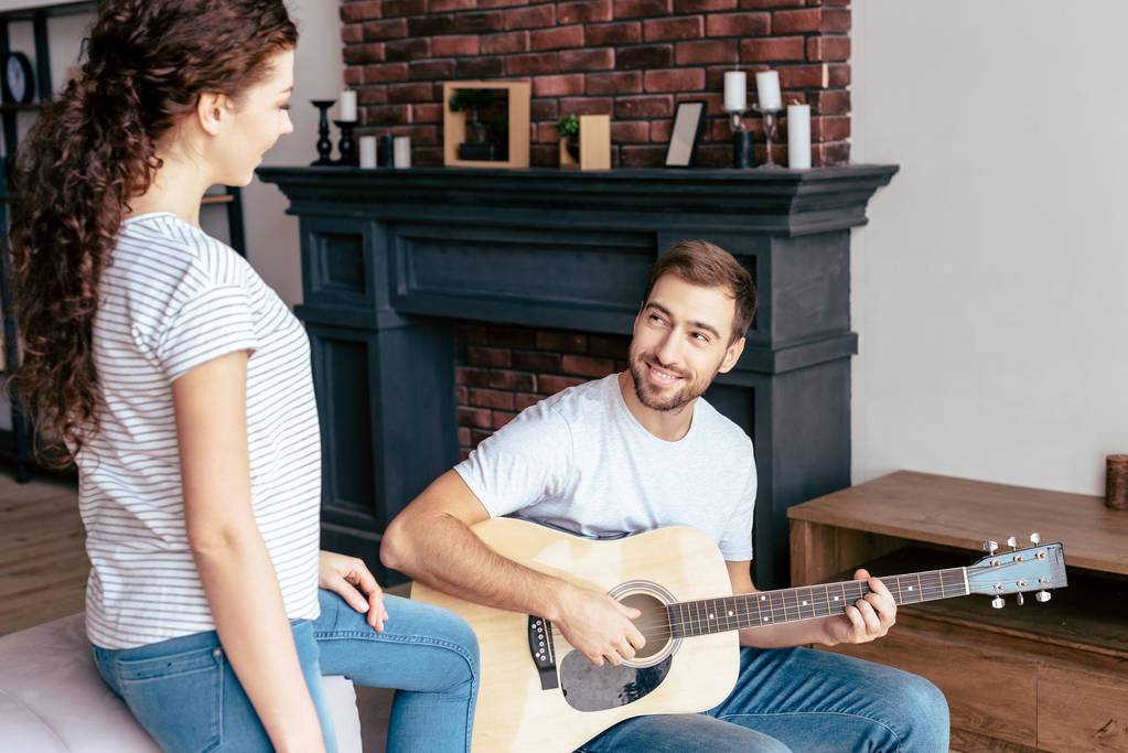 усміхнений бородатий чоловік грає на акустичній гітарі подрузі у вітальні
 - Фото, зображення