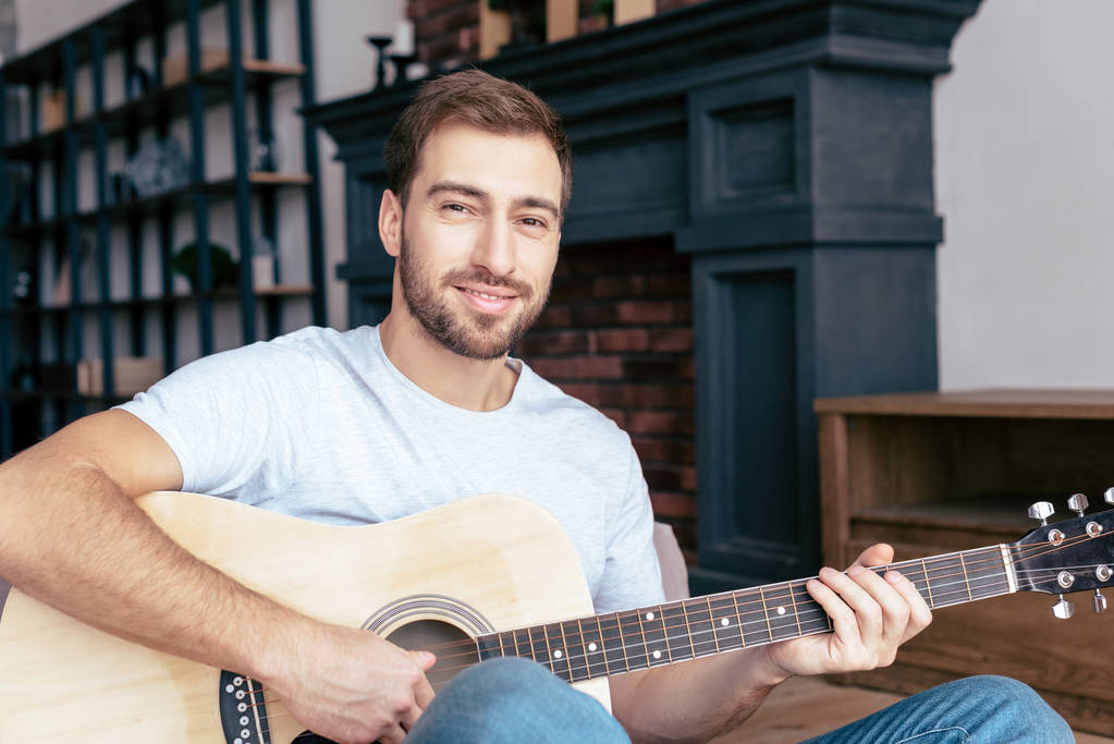 uomo barbuto sorridente che suona la chitarra acustica in salotto
 - Foto, immagini