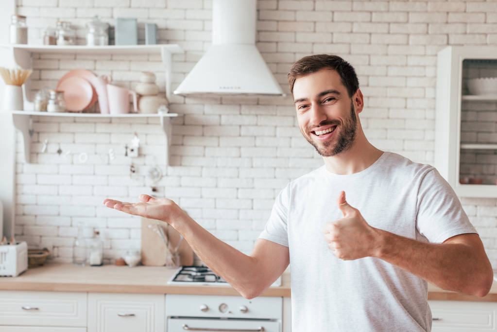 usměvavý vousatý muž ukazující palec nahoru a pohled na kameru - Fotografie, Obrázek