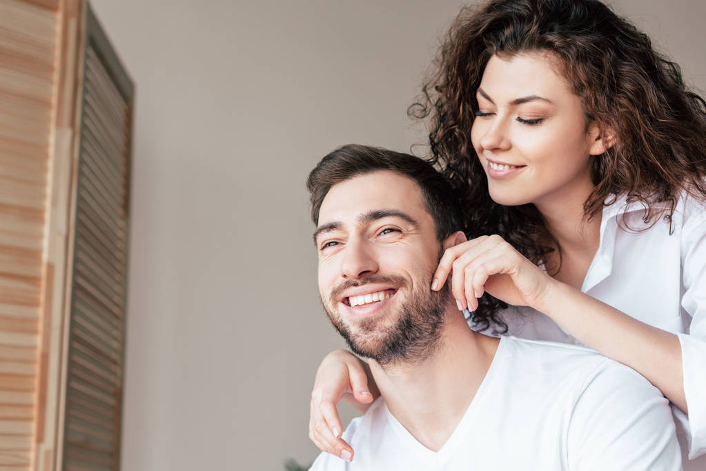 smiling curly young woman gently touching boyfriend at home - Photo, Image