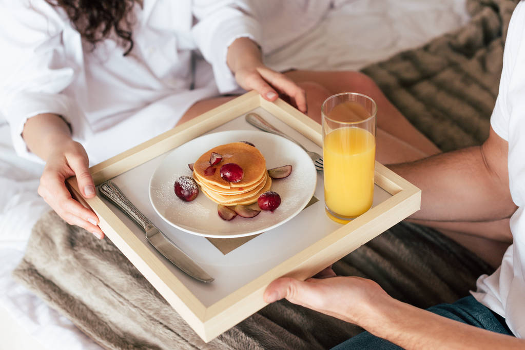 Teilansicht des Paares mit Tablett mit Pfannkuchen und einem Glas Orangensaft - Foto, Bild